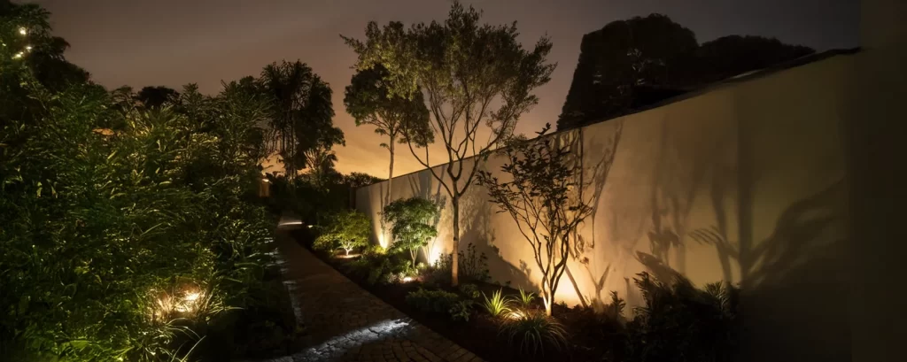 Jardim decorado com iluminação embutida e espeto LED entre arbustos e pedras, criando ambiente acolhedor e seguro à noite.